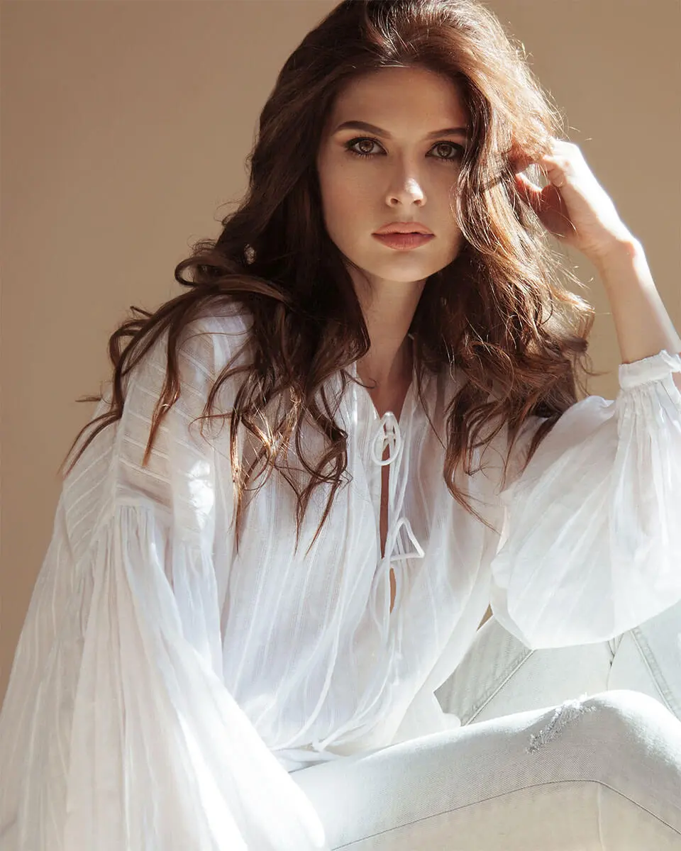 Model wearing white dress touching her face